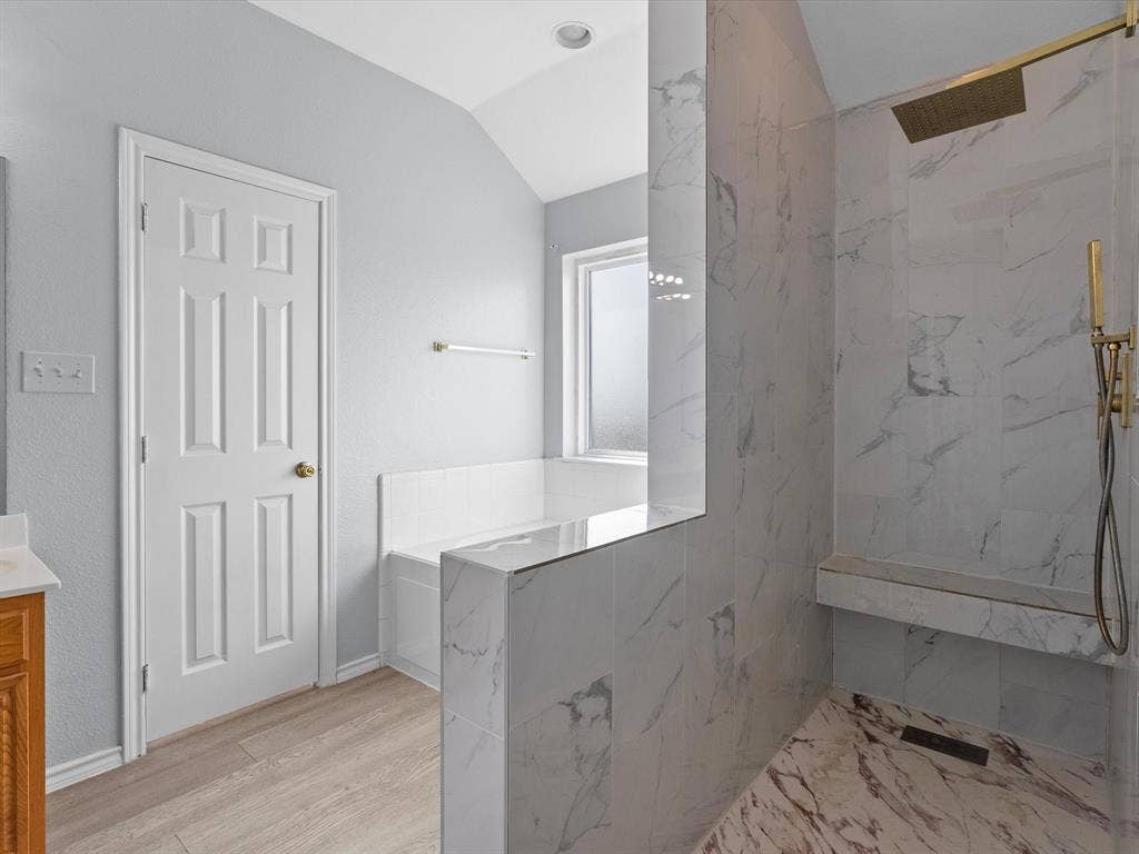 7302 San Carlos Drive, Rowlett, TX 75089 Walk-in shower with full-height tile surround, built-in bench, rain showerhead, and wall-mounted handheld shower fixture