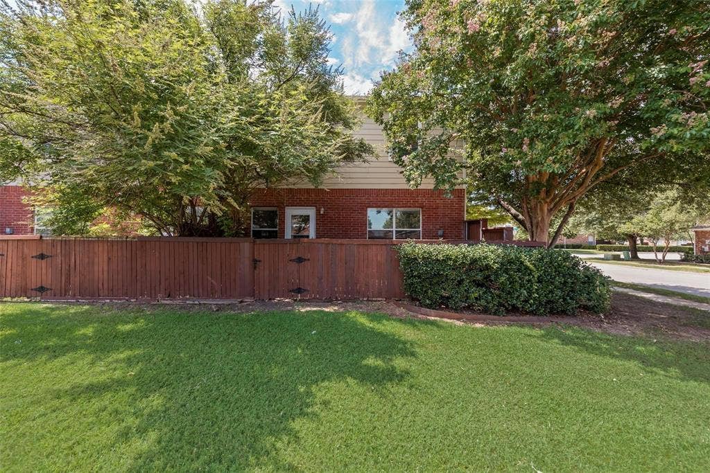 4541 Woodsboro Lane, Plano, TX 75024 Private fenced yard with lush green lawn, mature trees, and brick exterior