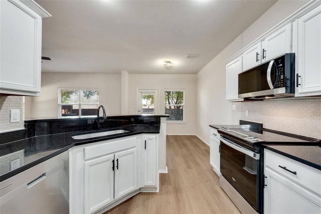 4541 Woodsboro Lane, Plano, TX 75024 Kitchen featuring dark countertops, white cabinetry with dark hardware, stainless steel appliances, and a tile backsplash