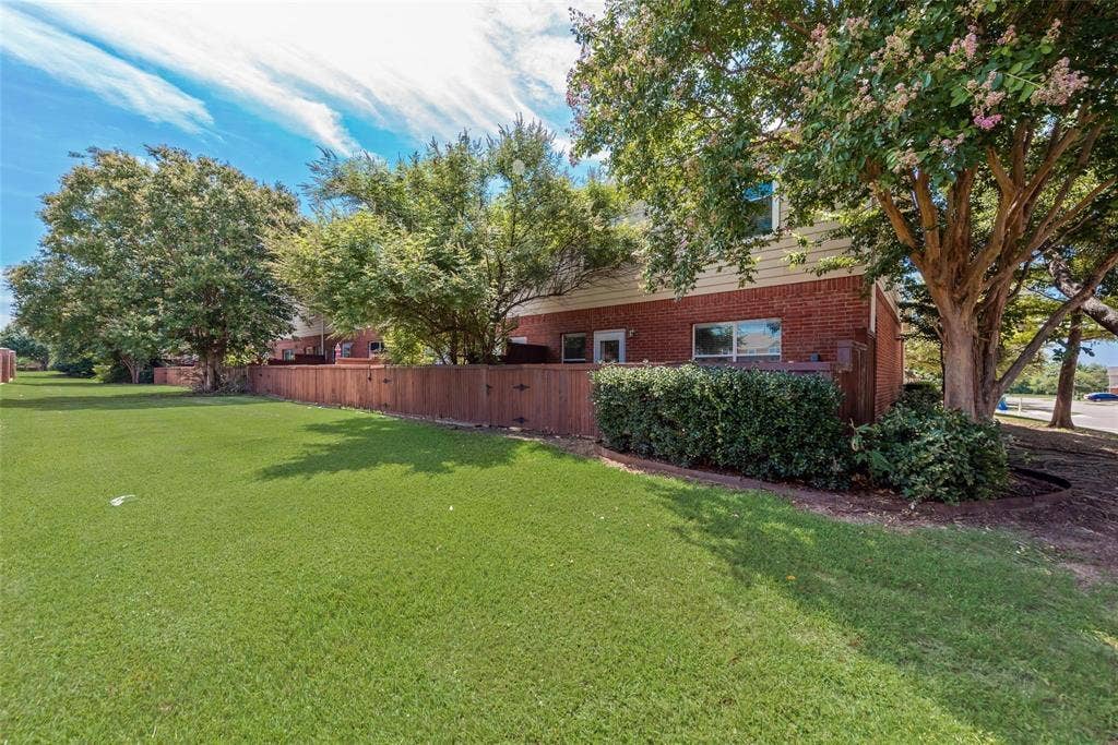 4541 Woodsboro Lane, Plano, TX 75024 Expansive lawn area with mature trees, established shrubbery, and a wood privacy fence