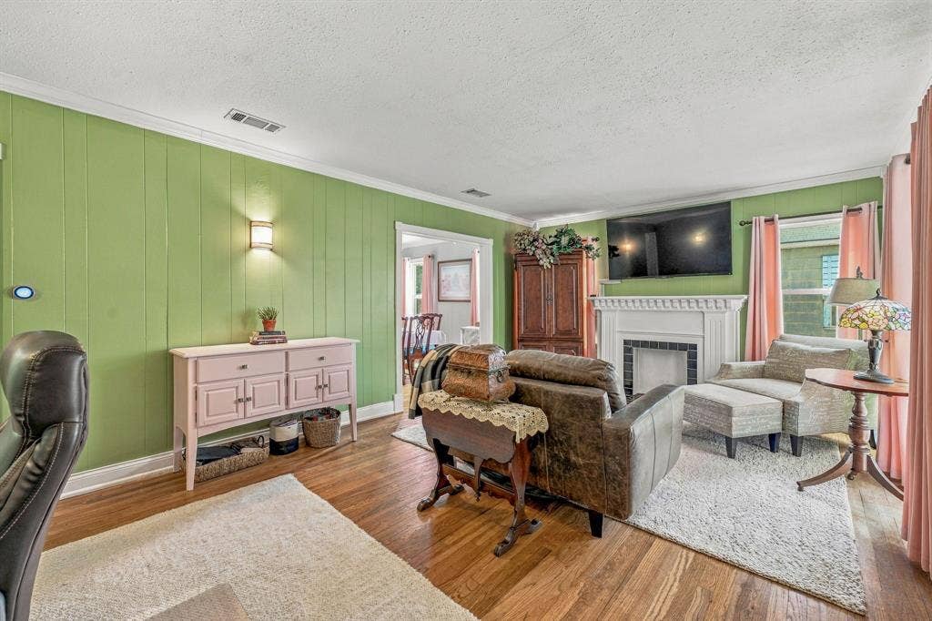Large living room with original hardwood flooring, faux fireplace and multiple windows to let in abundant natural light.