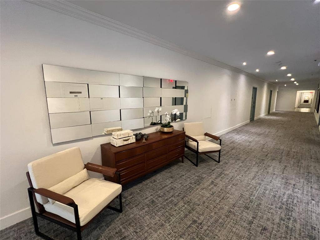 Hallway with crown molding, recessed lighting, wall-to-wall carpeting, and a decorative mirror installation