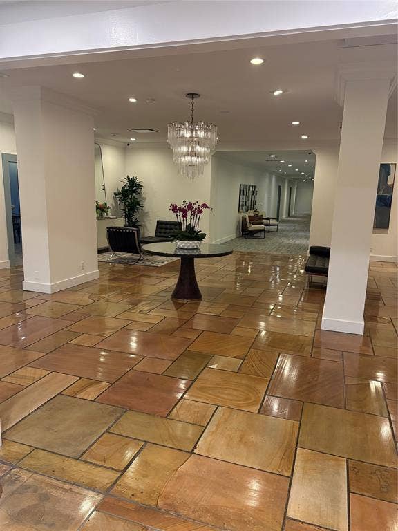 Polished stone tile flooring, recessed ceiling lighting, a decorative chandelier, and white architectural columns
