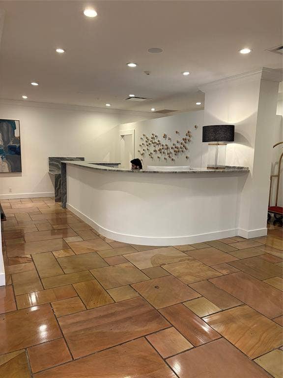 Curved reception counter with a stone-finish countertop, recessed lighting, and a patterned tile floor