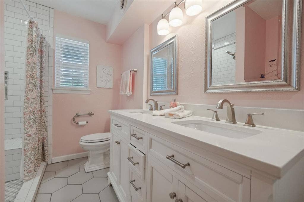 Primary Bathroom has remodeled vanity with double sinks, quartz countertop, recent hardware, comfort-height toilet, grab-bar toilet paper holder, handicap accessible shower with bench & grab bars, updated tile flooring.