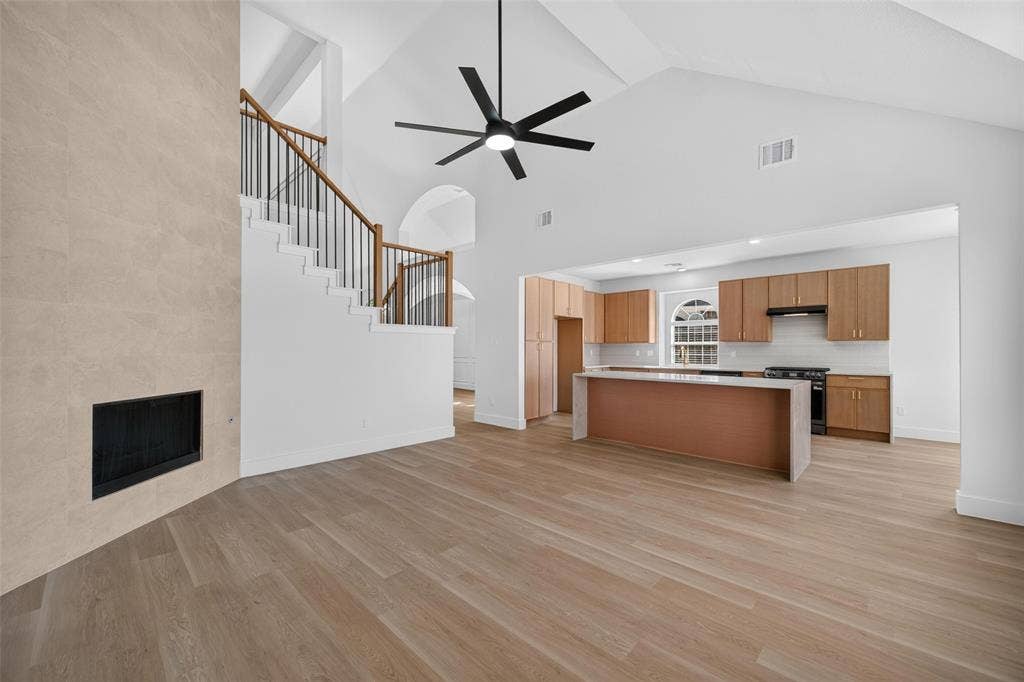 705 N Jordan Road, McKinney, TX 75071 Vaulted ceiling with an installed ceiling fan, wood-finish flooring, staircase with a wrought iron railing, fireplace with a tiled surround, and kitchen with an island and wood cabinetry