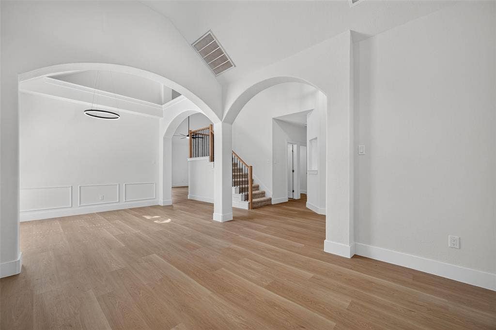705 N Jordan Road, McKinney, TX 75071 Wood-finish flooring, white walls, arched doorways, a built-in staircase with dark balusters, and a modern circular chandelier