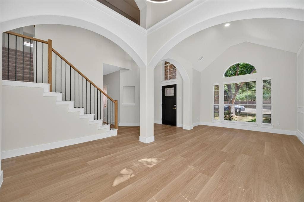 705 N Jordan Road, McKinney, TX 75071 Expansive interior featuring wood-finish flooring, vaulted ceilings, arched doorways, a grand staircase with wood handrails and wrought iron balusters, and large windows with transom arch detailing