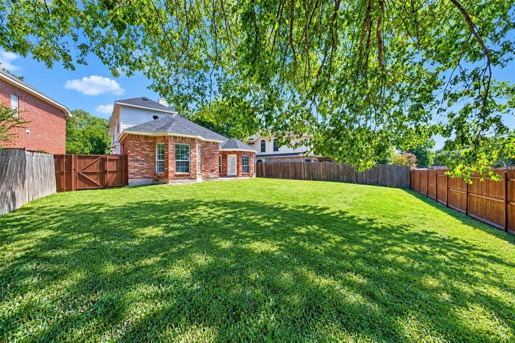 705 N Jordan Road, McKinney, TX 75071 Expansive backyard featuring a manicured lawn, full privacy fencing, mature trees, and a brick exterior with multiple windows