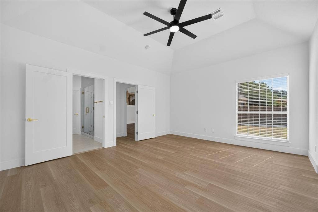 705 N Jordan Road, McKinney, TX 75071 Vaulted ceiling with a black ceiling fan, wood-finish flooring, a rectangular window, and two panel doors with gold-finish hardware
