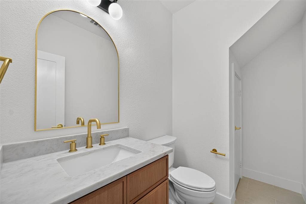 705 N Jordan Road, McKinney, TX 75071 Arched mirror with a brass frame, wood-finish vanity with a white countertop, and brass fixtures