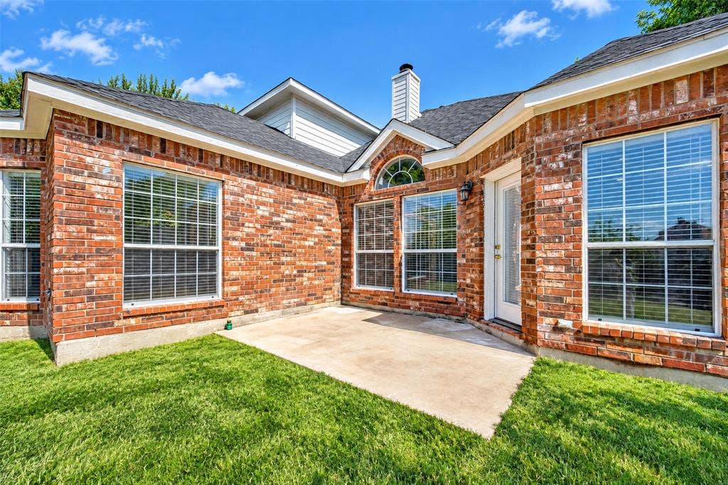 705 N Jordan Road, McKinney, TX 75071 Brick exterior with multiple windows, an arched transom window, a white door, and a concrete patio