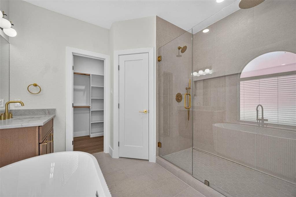 705 N Jordan Road, McKinney, TX 75071 Spacious bathroom featuring a glass-enclosed shower, freestanding soaking tub, single vanity with a marble-look countertop, and a walk-in closet with built-in shelving