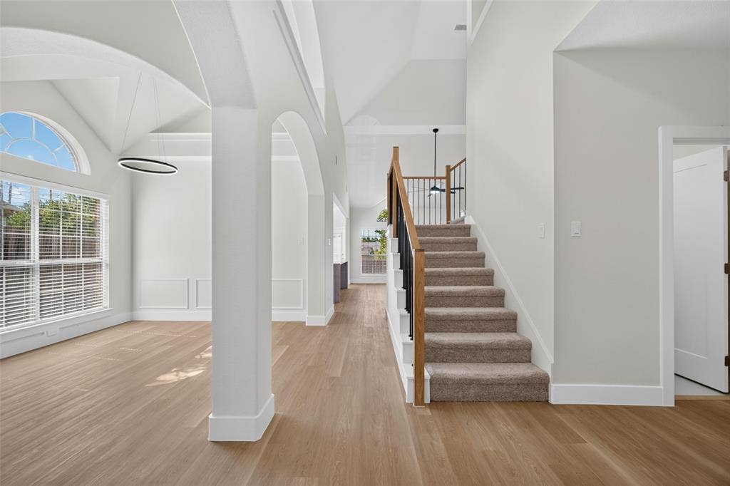 705 N Jordan Road, McKinney, TX 75071 Vaulted ceiling with an arched window, wood-finish flooring, staircase with carpeted treads and metal balusters, and a modern circular light fixture