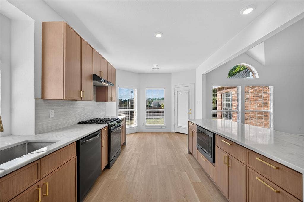705 N Jordan Road, McKinney, TX 75071 Contemporary kitchen featuring light wood-finish cabinetry, solid surface countertops, a stainless steel sink, and integrated black appliances