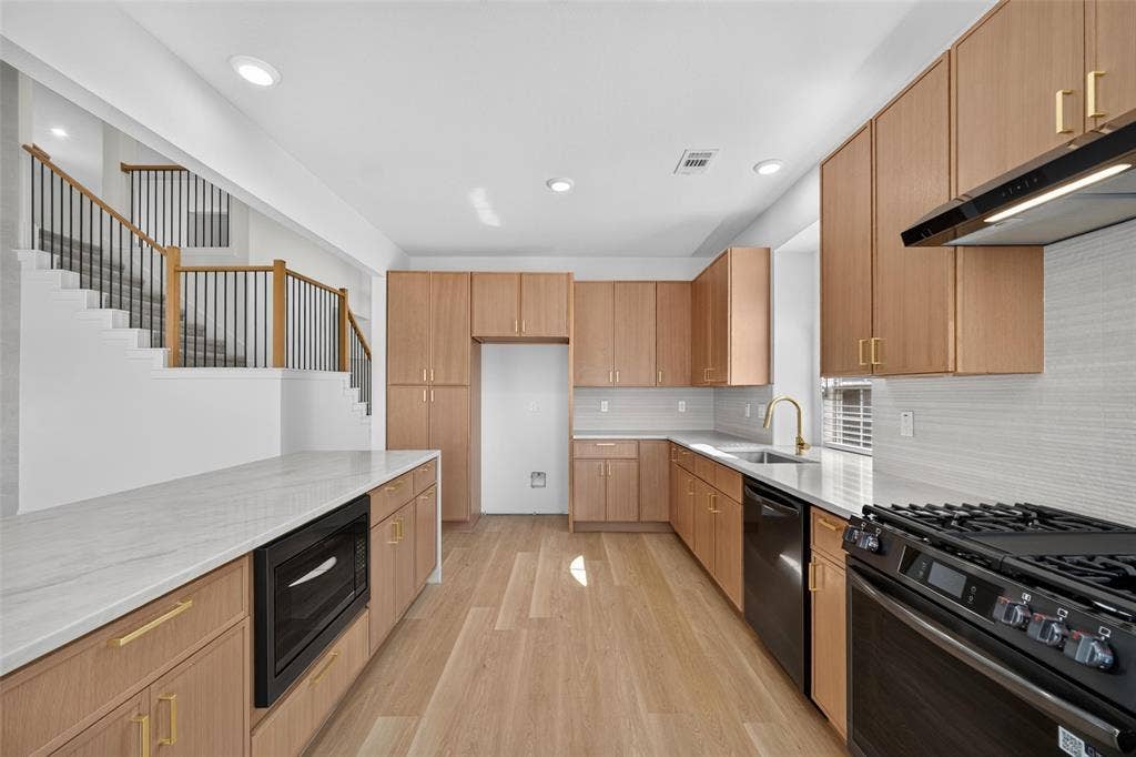 705 N Jordan Road, McKinney, TX 75071 White countertops, wood-finish flooring, light wood cabinetry, black appliances, and a staircase with wood handrails and black balusters