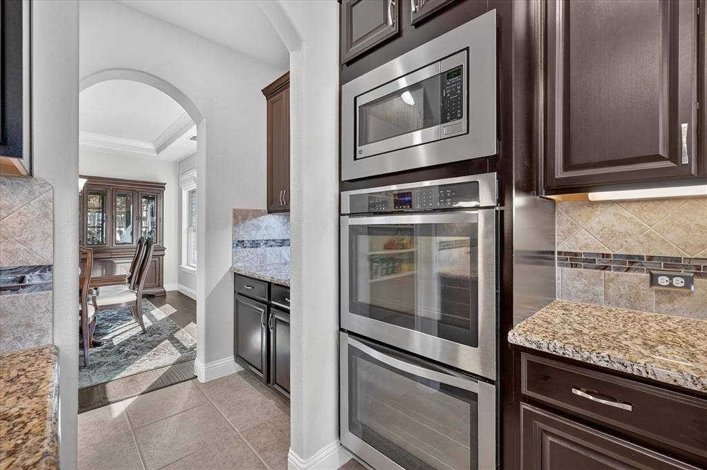 Built-in stainless steel double ovens, rich wood-finish cabinetry, granite countertops, and tiled backsplash