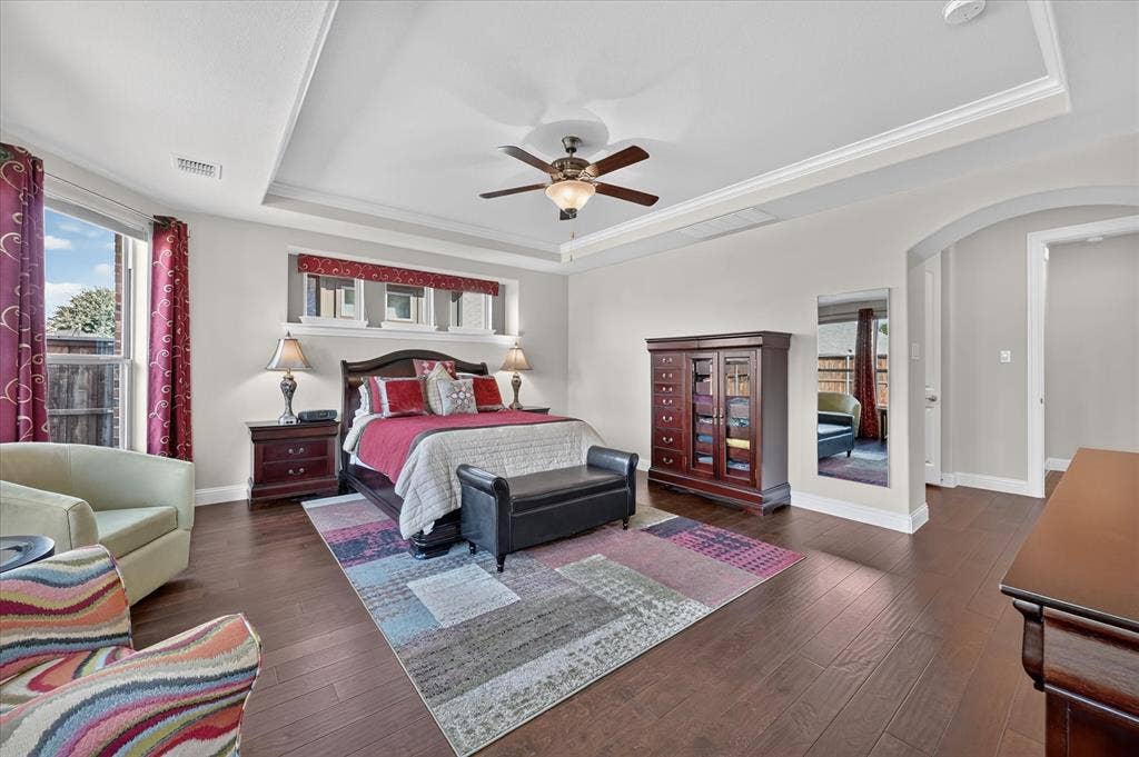 Tray ceiling with a ceiling fan, wood-finish flooring, arched doorway, and multiple windows