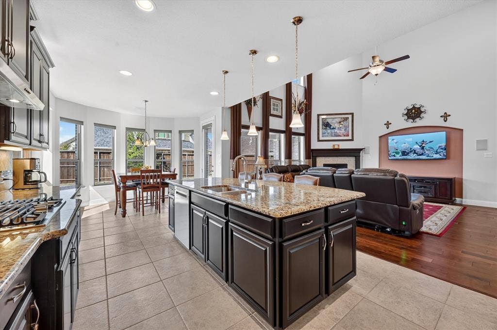Kitchen with dark wood-finish cabinetry, granite countertops, a center island with sink, and tile flooring