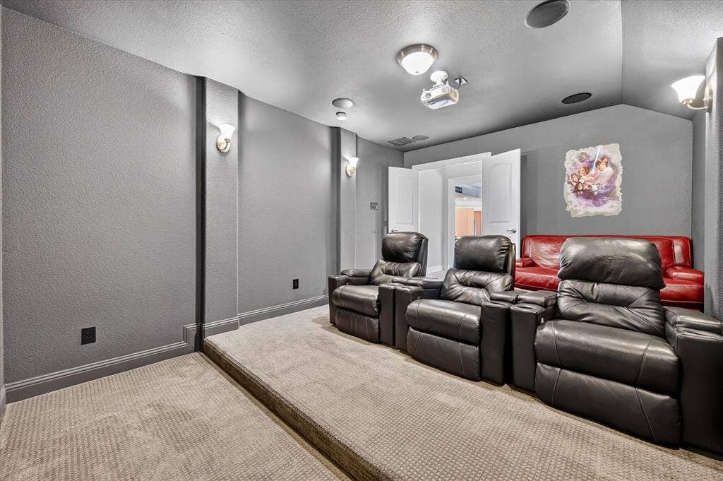 Dedicated media room featuring tiered carpeting, recessed lighting, and wall sconces