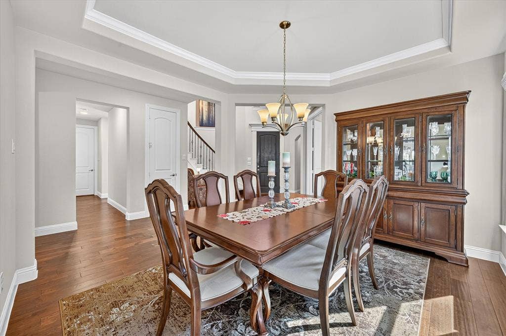 Tray ceiling with crown molding, wood-finish flooring, chandelier lighting, and a built-in display cabinet