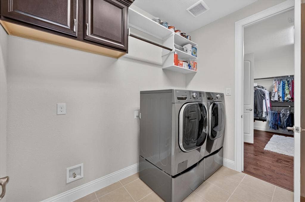 Laundry area featuring dark wood-finish cabinetry, open shelving, and light-toned tile flooring