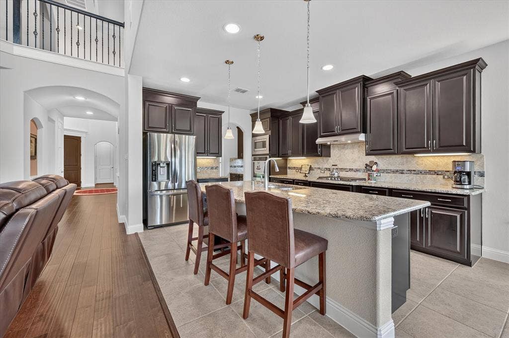 Kitchen featuring dark wood cabinetry, a large kitchen island with a light-toned countertop, stainless steel appliances, and tile flooring