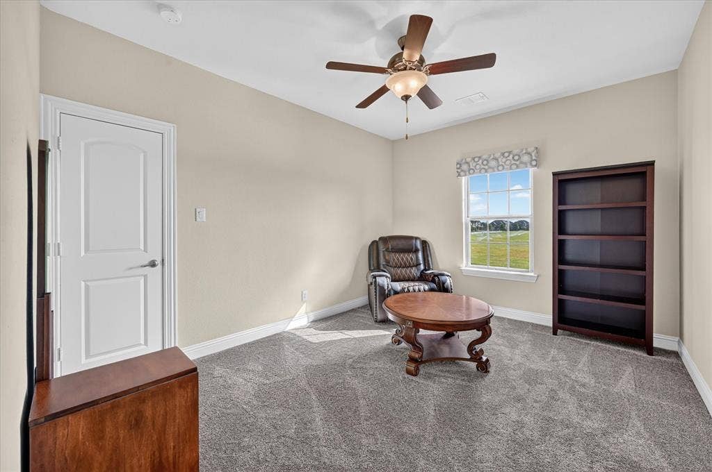 Carpeted room featuring a ceiling fan with light fixture, a window with a patterned valance, and a white interior door