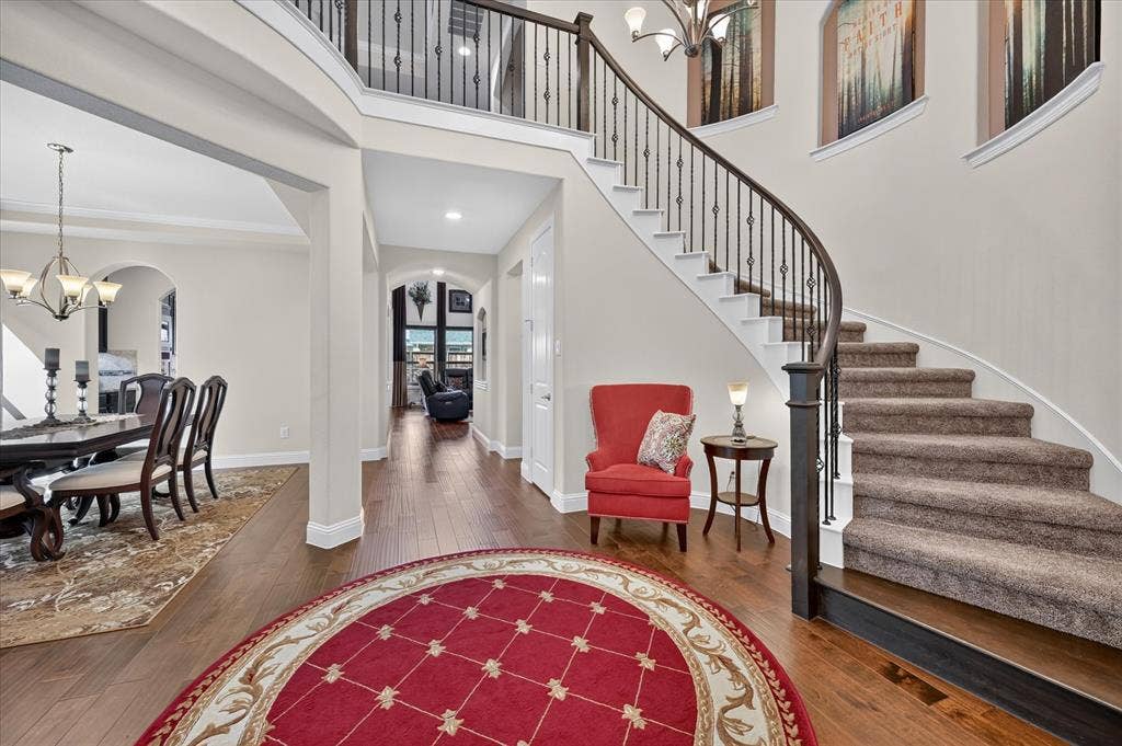 Swooping staircase with wrought iron balusters, wood-finish flooring, and arched doorways