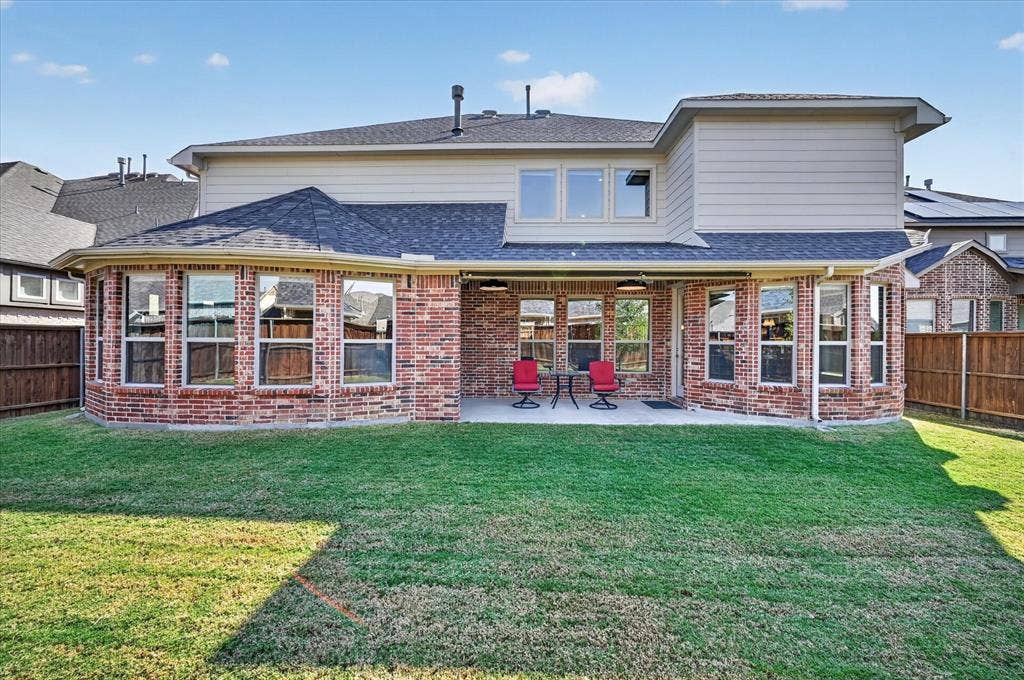 Rear exterior featuring a brick and siding facade with multiple windows, a covered patio, and a grass lawn