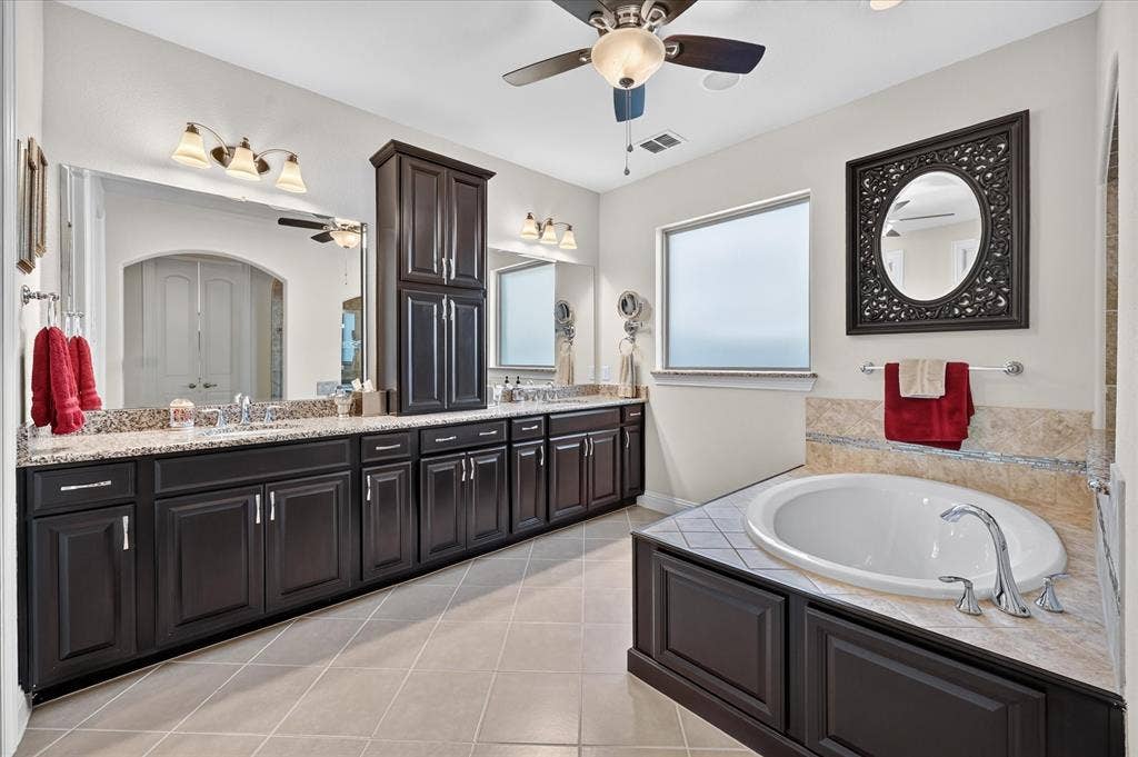 Dual vanity with granite countertops, extensive cabinetry, built-in soaking tub, and tile flooring