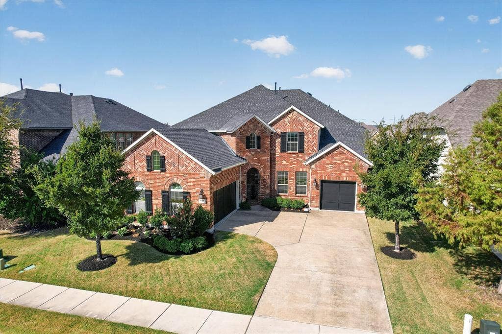 Brick exterior with dark shingle roofing, black shutters, and an attached two-car garage