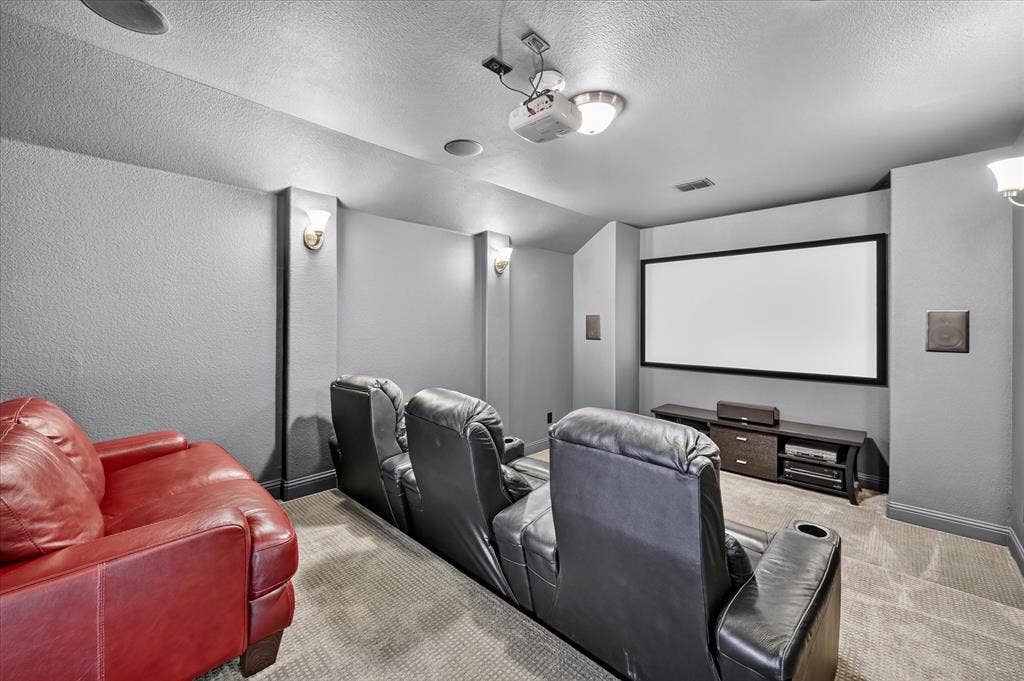 Dedicated media room featuring a large projection screen, wall-mounted speakers, recessed ceiling lighting, and sconce lighting