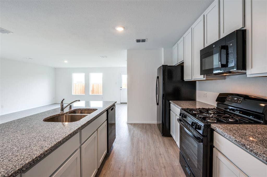 1708 Sims Street, McKinney, TX 75071 Kitchen with black appliances, white cabinetry, stone countertops, sink, and light hardwood / wood-style flooring