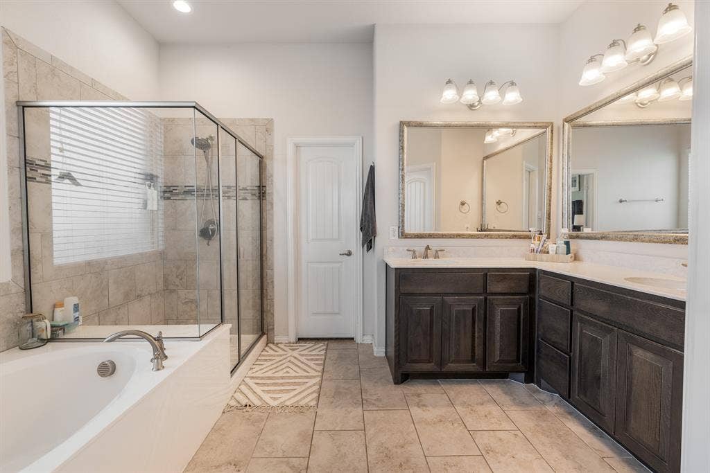 3605 Barby Court, Midlothian, TX 76065 Tiled flooring throughout, dual wood-finish vanity with countertop, framed mirrors, glass-enclosed shower, and built-in soaking tub