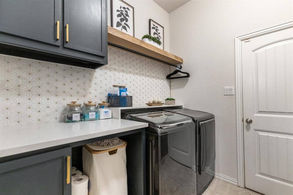3605 Barby Court, Midlothian, TX 76065 Laundry area featuring dark cabinetry with gold-toned hardware, a white countertop, patterned tile backsplash, and a wood-finish floating shelf