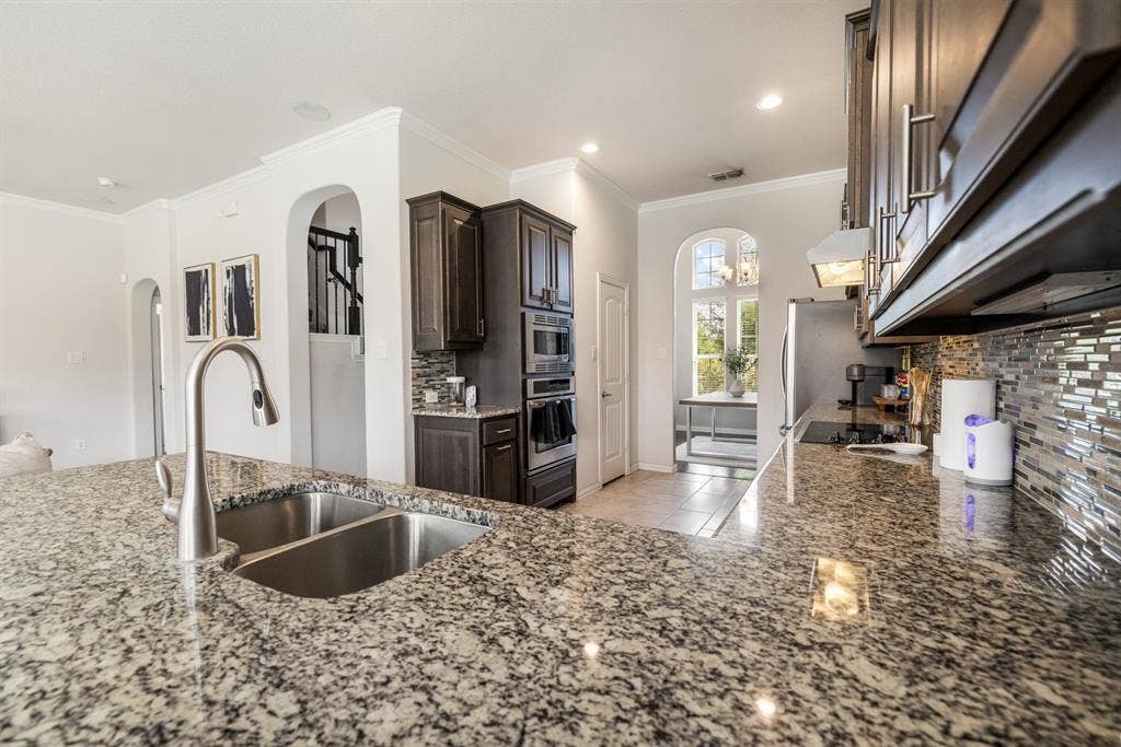 3605 Barby Court, Midlothian, TX 76065 Kitchen featuring granite countertops, a double basin stainless steel sink, dark wood cabinetry, stainless steel appliances, and a tiled backsplash