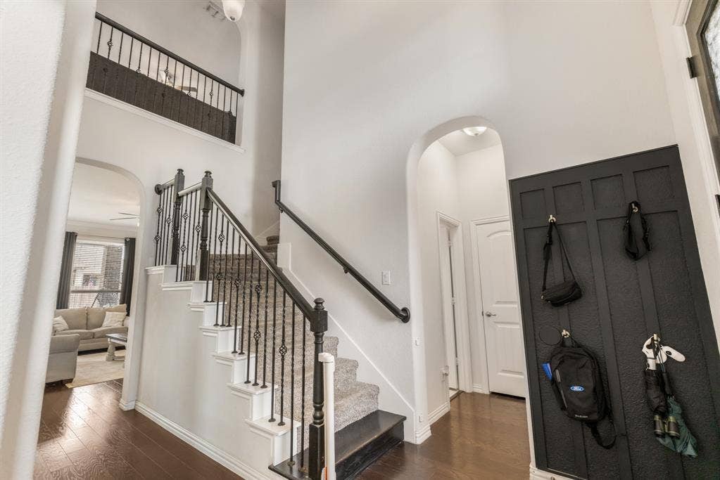 3605 Barby Court, Midlothian, TX 76065 Foyer featuring wood-finish flooring, a carpeted staircase with ornate iron balusters, an arched doorway, and wainscoting
