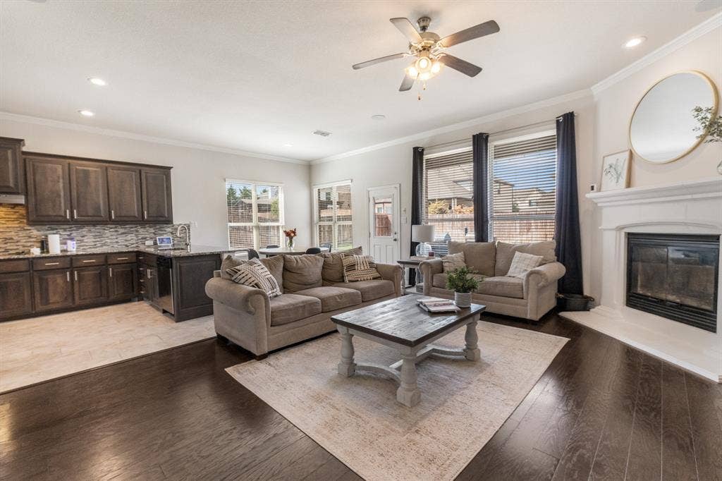 3605 Barby Court, Midlothian, TX 76065 Open-concept living area featuring rich wood-finish flooring, a contemporary ceiling fan with integrated lighting, and a fireplace with a white mantel
