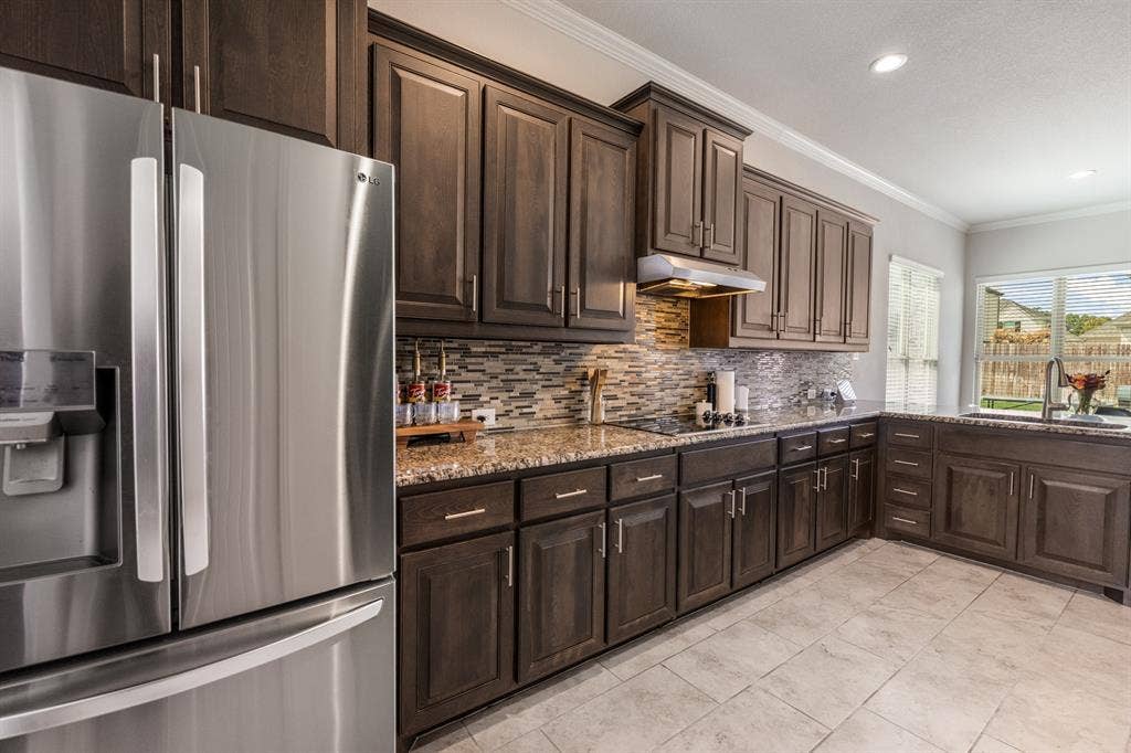 3605 Barby Court, Midlothian, TX 76065 Stainless steel refrigerator, dark wood cabinetry, patterned tile backsplash, light-colored tile flooring, and a large window above the sink