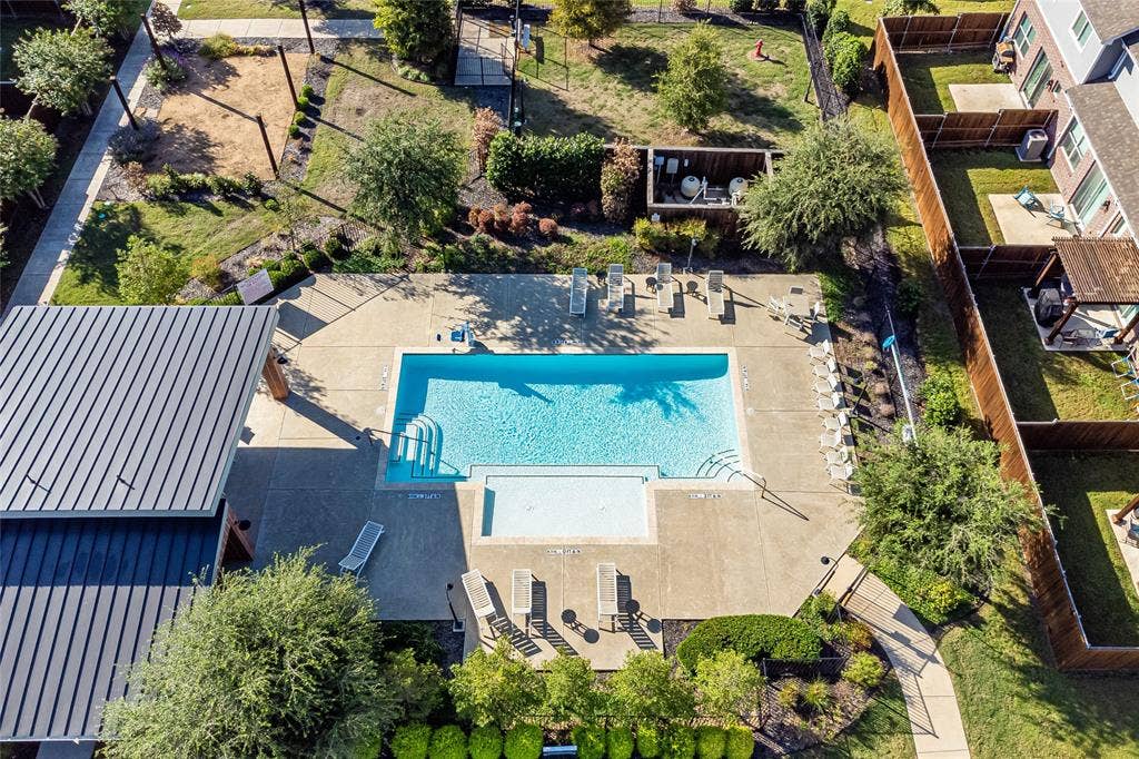 Swimming pool with a baja shelf, concrete deck, metal roof structure, and perimeter landscaping