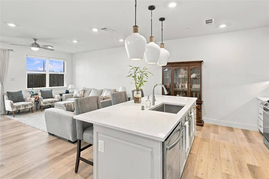 Kitchen island with quartz countertop and undermount stainless steel sink, wood-finish flooring, recessed lighting, and trio of pendant lights