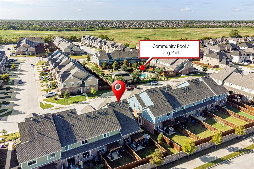 Aerial perspective of multi-family residential structures featuring shingle roofs, wood-fence enclosed private yards, and community amenities including a swimming pool and pet park