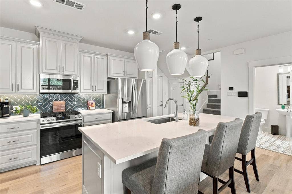 Kitchen featuring white shaker-style cabinetry, quartz countertops, herringbone-pattern tile backsplash, stainless steel appliances, and three glass pendant lights over the central island