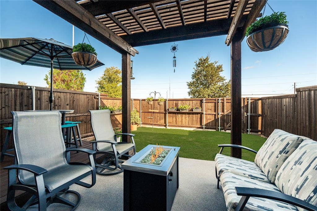 Outdoor patio featuring a wooden pergola, privacy fencing, and turf lawn