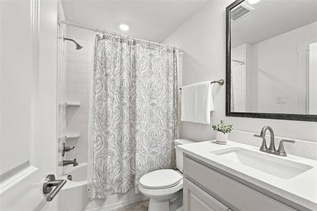 Bathroom featuring a vanity with a white countertop and rectangular undermount sink, framed mirror, and a tub-shower combination with white tile surround