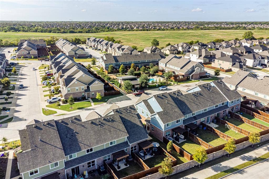 Aerial perspective of residential community featuring multi-story dwellings, fenced backyards, paved roadways, mature landscaping, and a central swimming pool