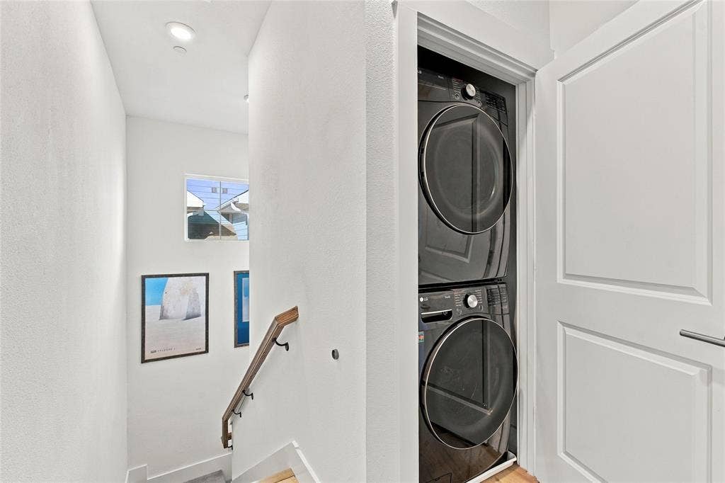 Laundry closet featuring a stacked washer and dryer, recessed lighting, and a wood-finish handrail with black iron hardware