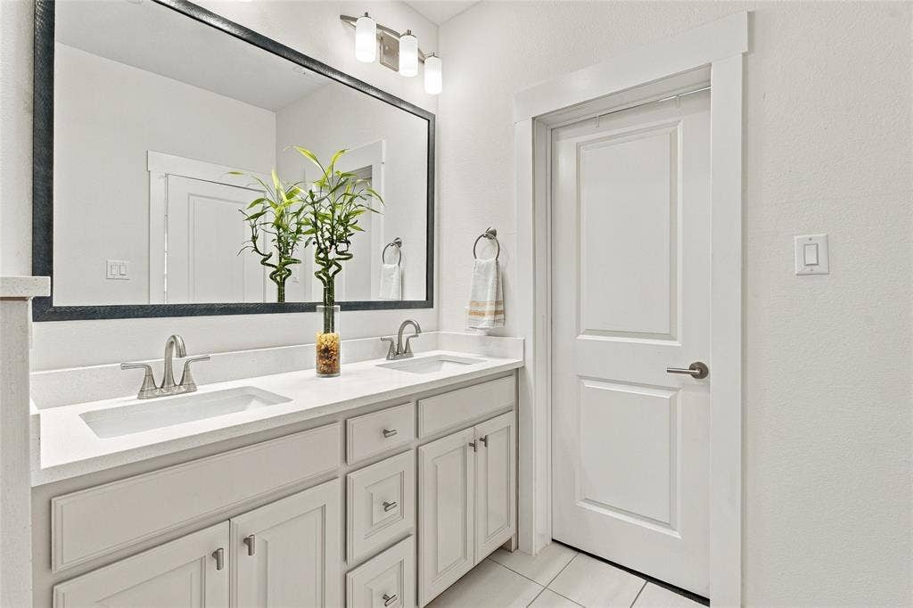 Dual-sink vanity with a solid-surface countertop, large framed wall mirror, polished chrome fixtures, and shaker-style cabinetry