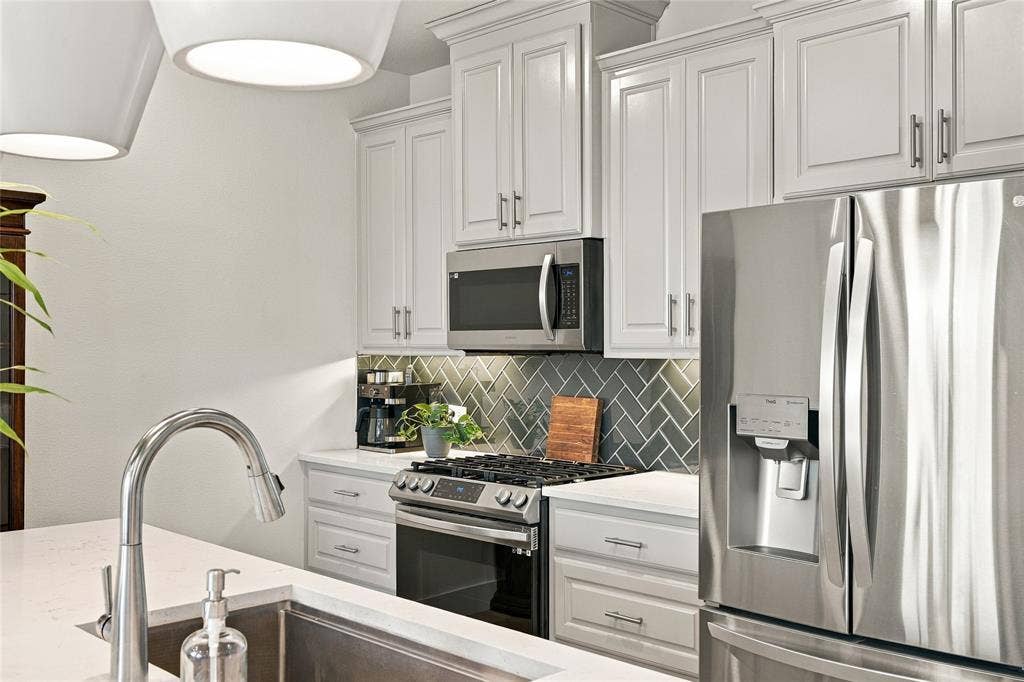 Kitchen featuring white shaker-style cabinetry, stainless steel appliances, quartz countertops, a herringbone-patterned tile backsplash, and a high-arc faucet